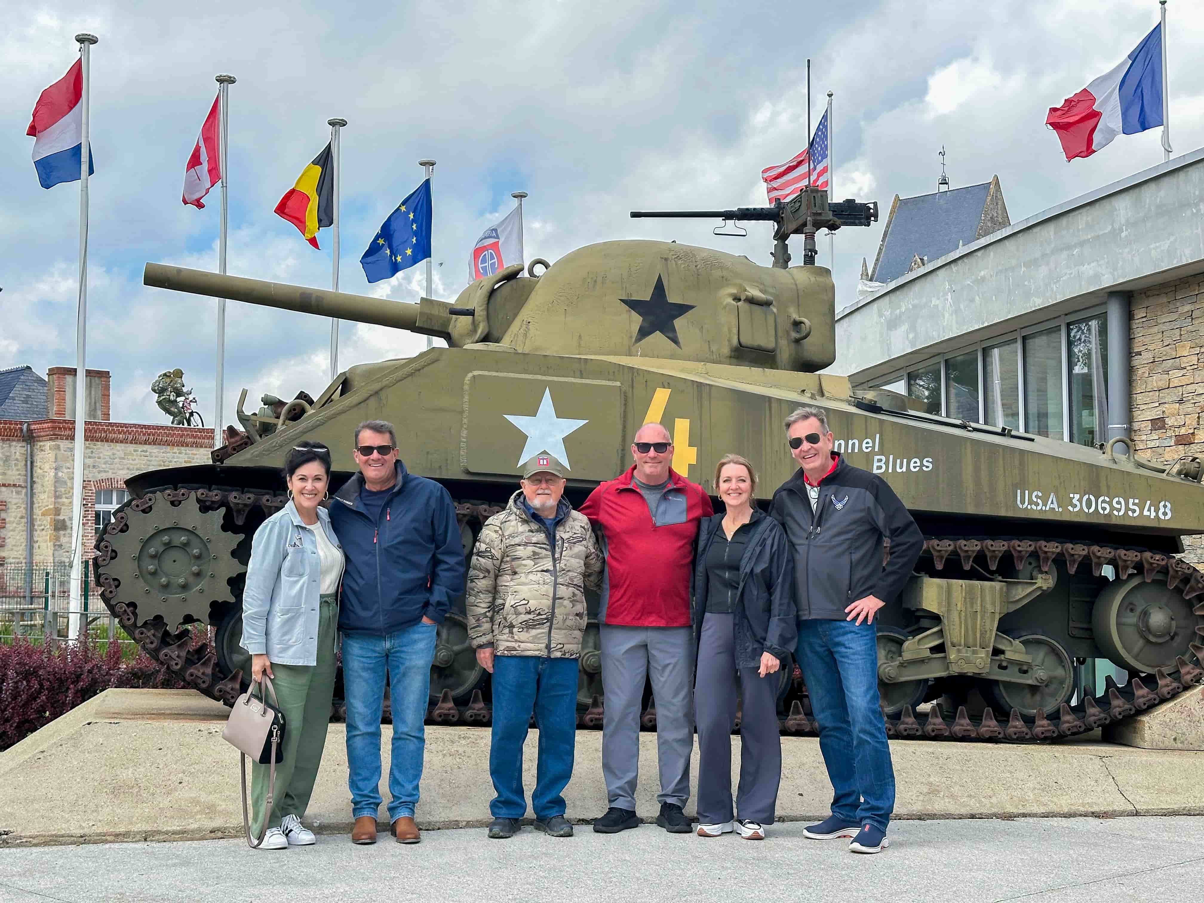 Small-group tour posing with a Sherman tank and Allied flags on a 2025 Normandy D-Day tour