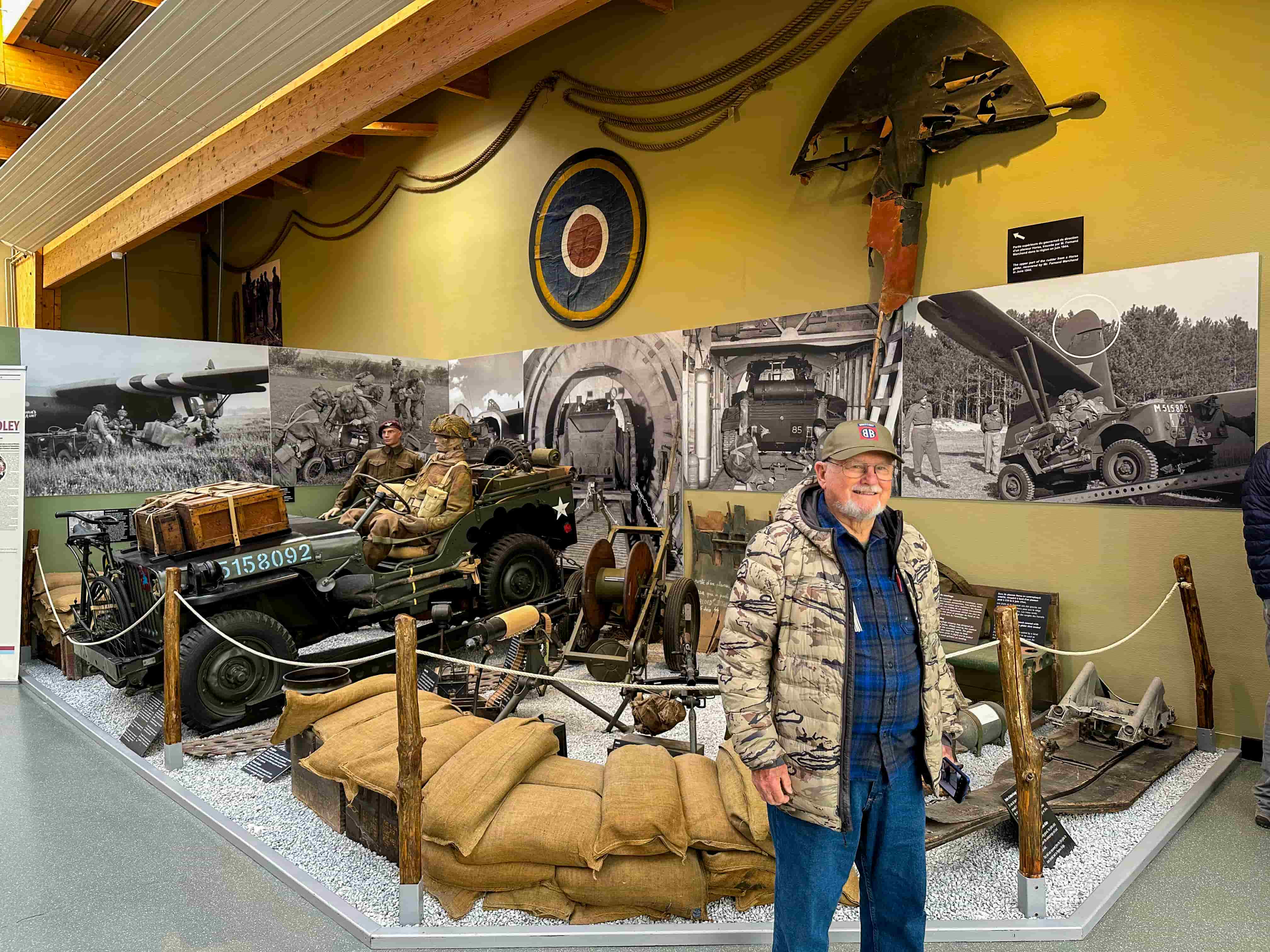Traveler beside a restored WWII jeep and airborne display in a Normandy D-Day museum