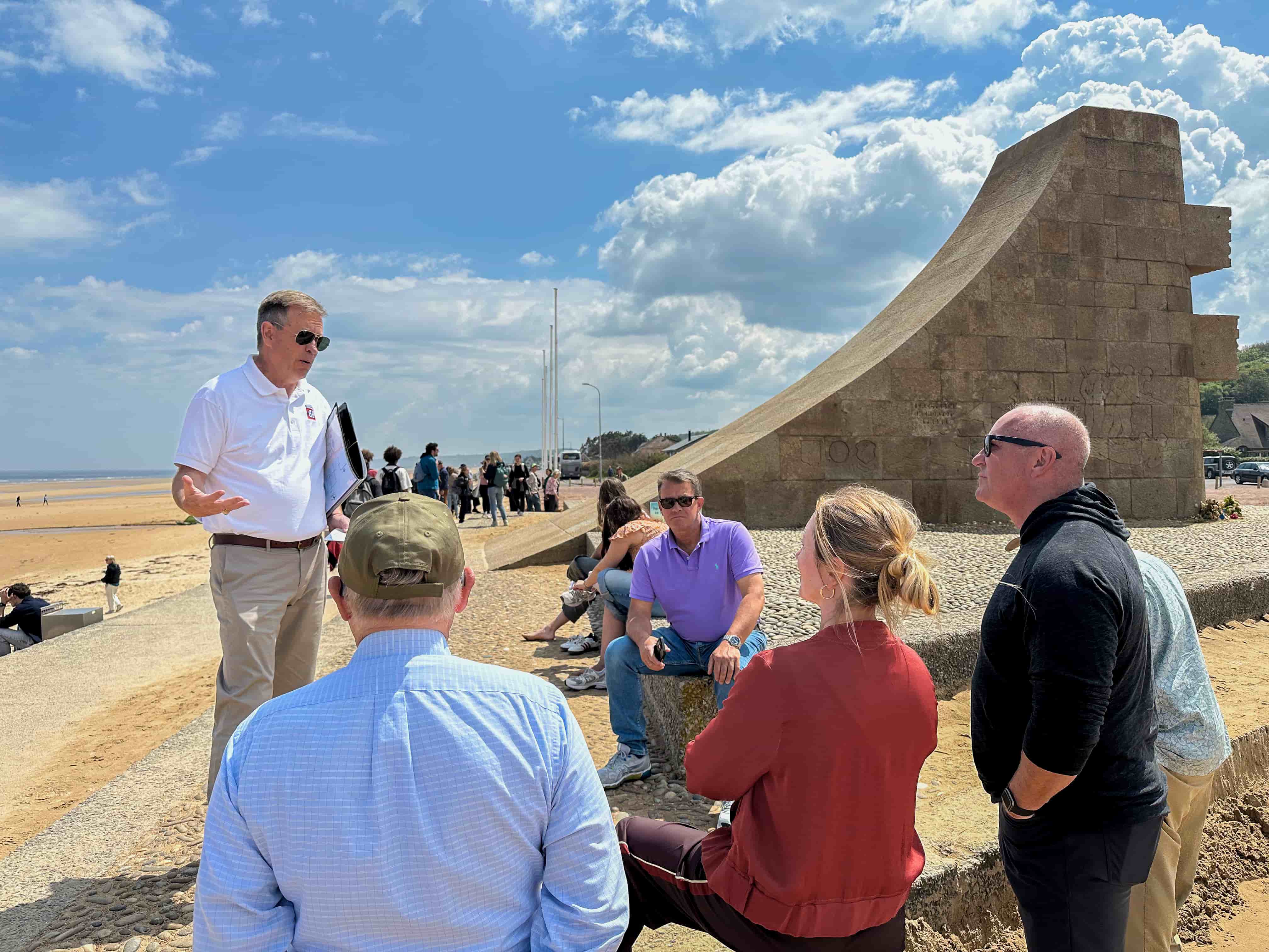 Guide briefing the small group beside a memorial on Omaha Beach, Normandy