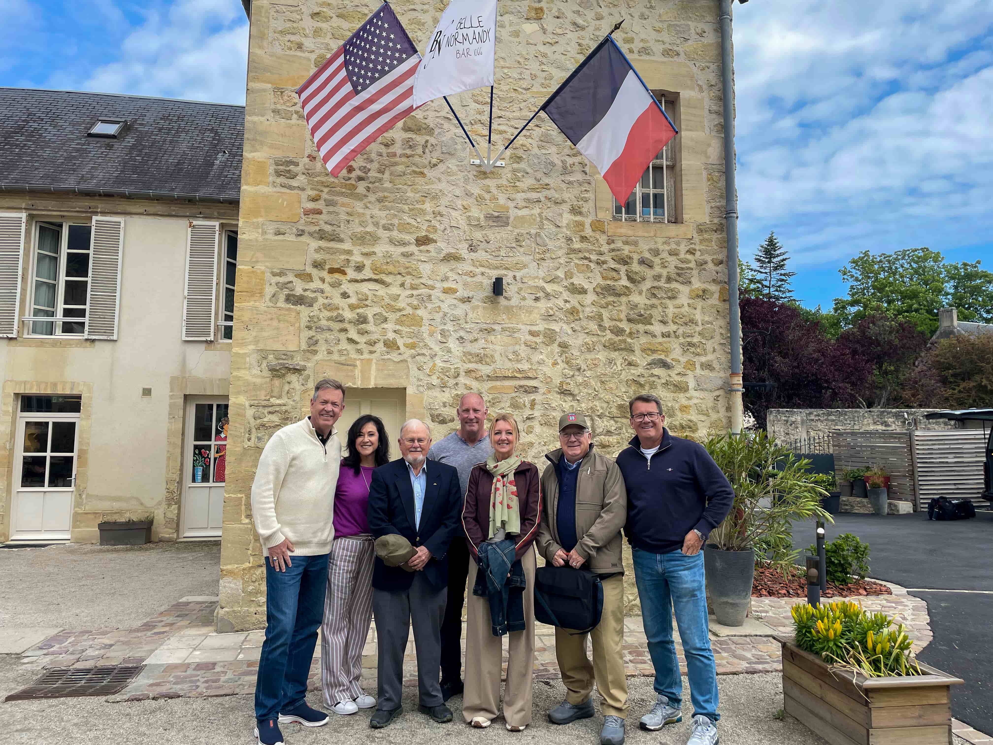 Small-group tour outside their Normandy hotel beneath US and French flags