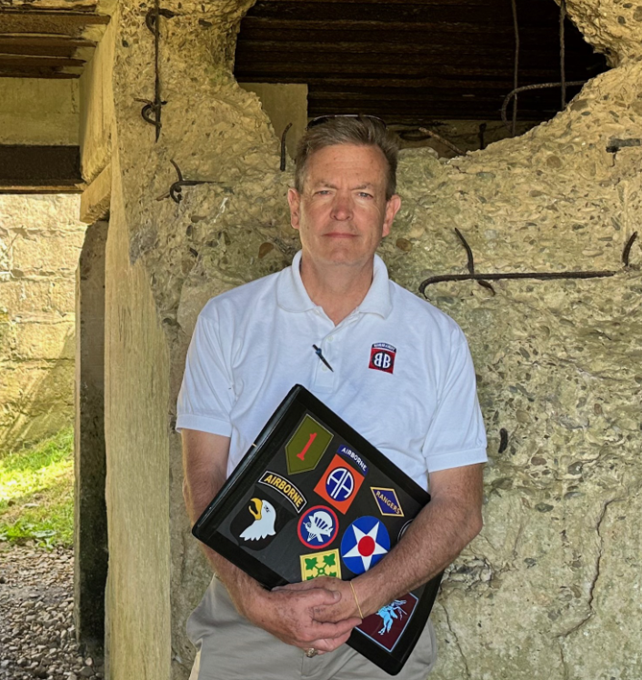 Joe McGrath, retired USAF Lieutenant Colonel, in a Normandy gun casemate holding a binder of WWII unit patches