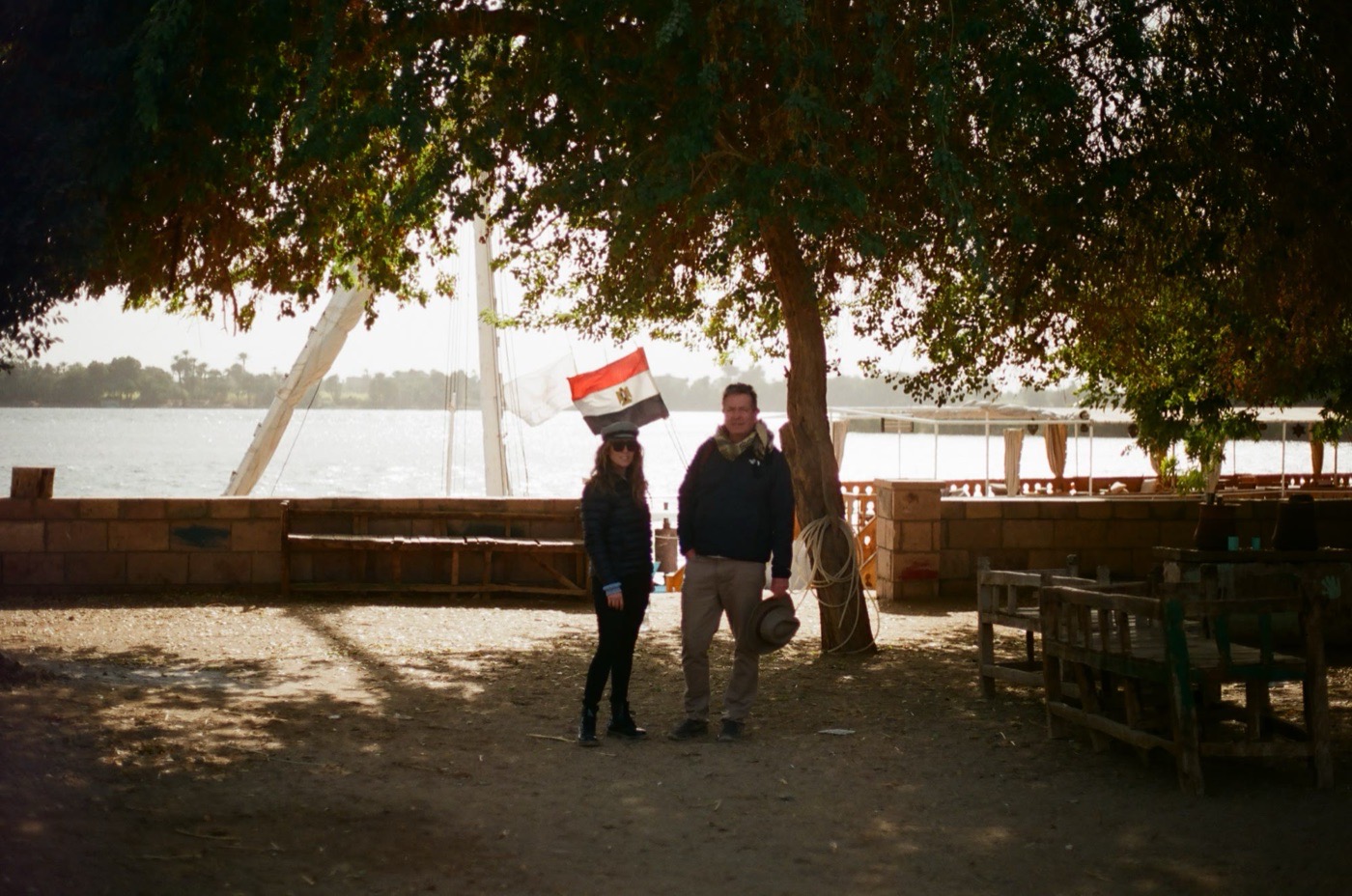 Travelers on the bank of the Nile beside a moored felucca and the Egyptian flag