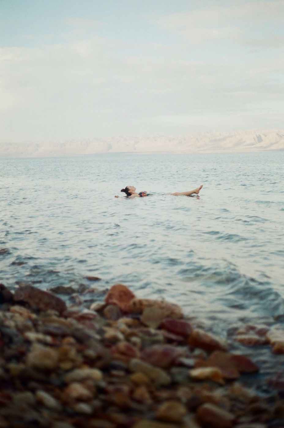 A lone swimmer floating off the pebble shore of the Dead Sea