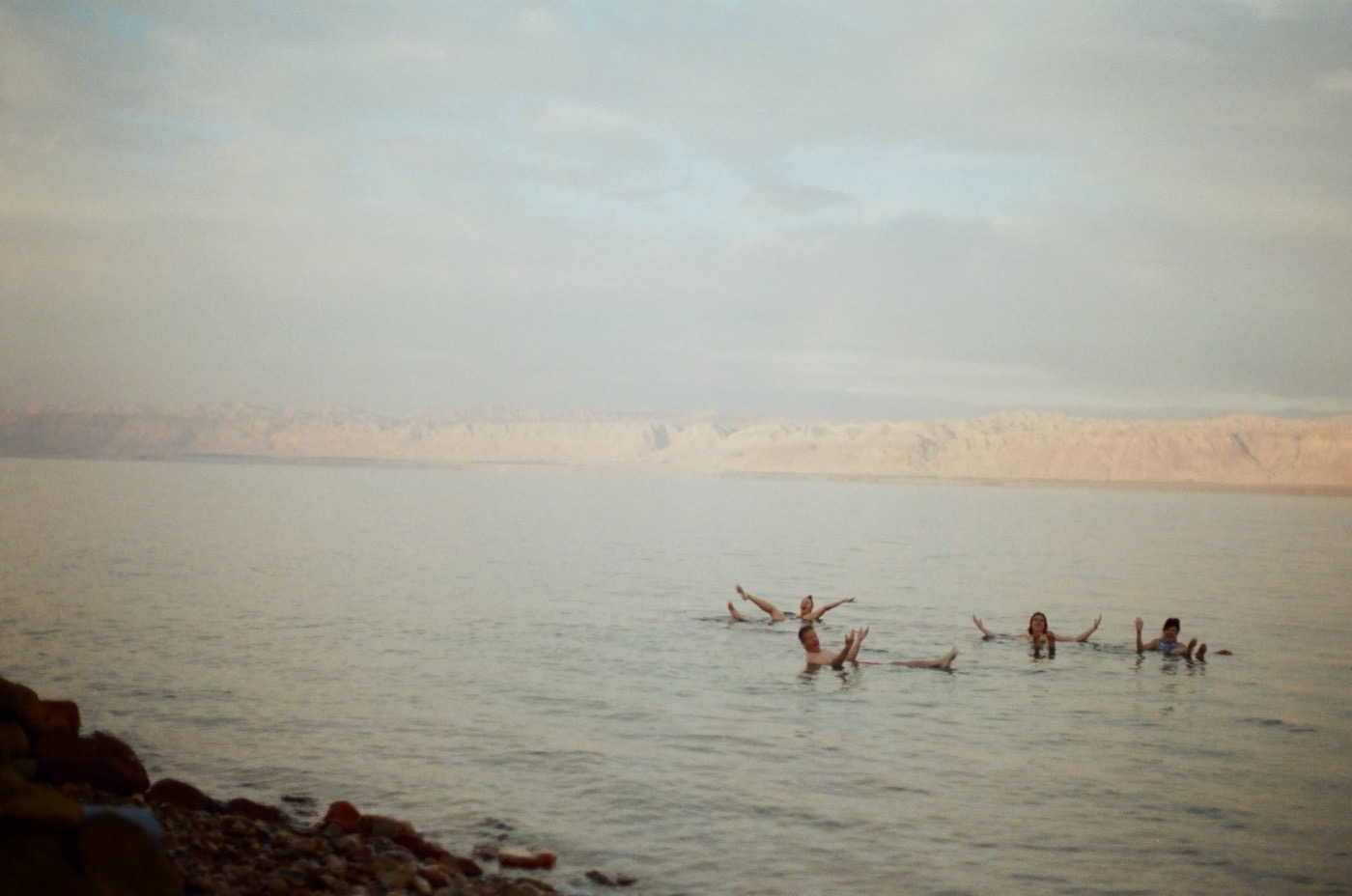 Travelers floating in the Dead Sea with the hills of the far shore behind them