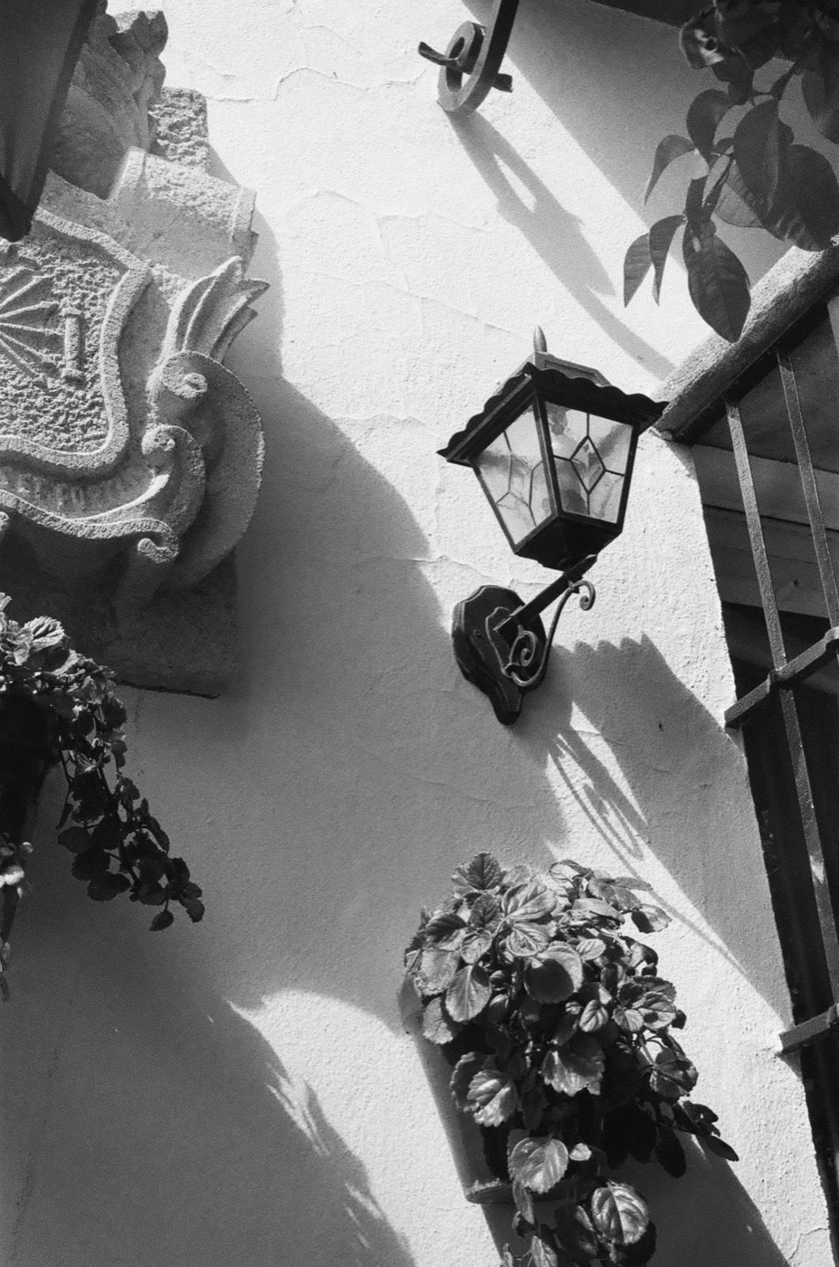 A wrought-iron lantern and its shadow on a whitewashed Andalusian wall, shot on black and white film