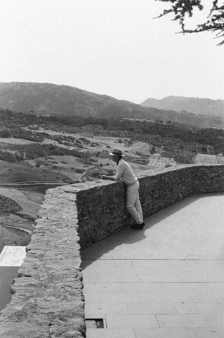 A traveler resting on a clifftop wall above the valley at Ronda, shot on black and white film